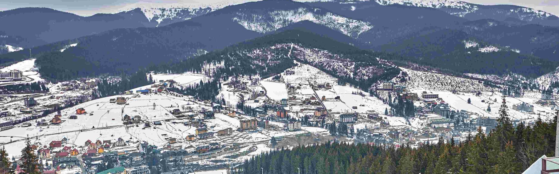 compressed_panorama-ski-resort-slope-people-ski-lift-skiers-piste-green-pine-trees-snow-lances-copy-space